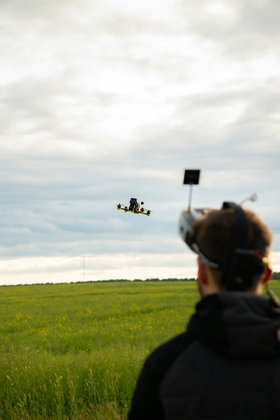 Person flyger en racingdrönare i en molnig himmel.